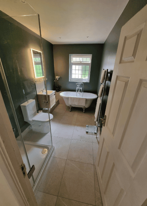 A roll-top bath against deep green walls, with a walk-in shower enclosure and stone-tiled floor.