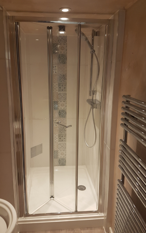 A shower enclosure with a mosaic feature strip, bi-fold glass door and chrome towel radiator.